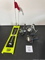 Photo showing four fishing reels and a yellow measuring tool with a metal spring mechanism and red flag on black surface.