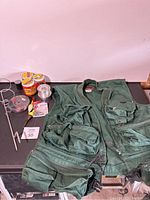 Fishing vest laid out flat showing multiple pockets and zipper closure with fishing accessories around it including fishing line spools, bobber floats, hooks, and small tackle case.