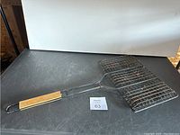 Full view of the metal grilling basket showing wire mesh basket and wooden handle on black surface.