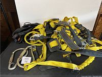 Photo showing full view of the yellow and black harness with carabiners and yellow rope spread out on black surface.