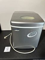 Front angle view of silver Salton ice maker with visible power cord and top viewing window.
