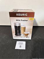 Front view of boxed Keurig Milk Frother showing brand, product image, and key features.