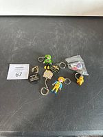 Photo showing seven assorted keychains laid out on a dark surface including figurine and commemorative keychains