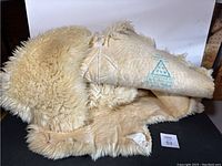 Full view of cream colored lamb skin blanket showing fleece side and suede leather side with natural irregular edges.