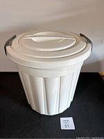 Front angled view showing whole white plastic can with lid and black locking handles.