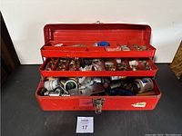 Front view of opened red metal toolbox filled with plumbing fittings and parts organized in three tiers.
