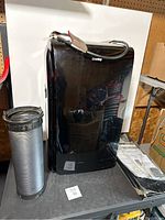 Danby black portable air conditioner shown with a flexible exhaust hose on the side, placed on a metal surface.