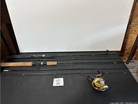 Photo showing three fishing rods and one reel set on a black surface.