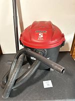 Shop Vac wet/dry vacuum in red and black with flexible hose and wand.
