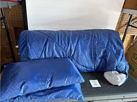 Sleeping bag displayed draped over a bench, with two small pillows placed next to it, all in dark blue with diamond pattern.