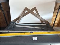 Two metal carpenter squares, two hand saws, and yellow Mastercraft ruler on black chest.