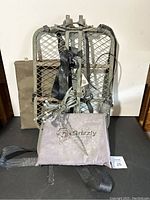 Front view of the entire Grizzly tree stand, safety harness straps, carrying bag placed behind, and sharpener rod with chain coiled on the bag.