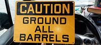 Full view of the vintage warehouse sign showing the entire text 'CAUTION GROUND ALL BARRELS' in black on yellow metal.