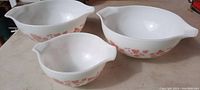 Set of three vintage Pyrex mixing bowls with pink flower design, showing all three bowls from an angled front view.
