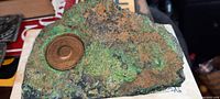 Top-down view showing rough textured copper ore with green and blue oxidization, embedded bronze identification badge