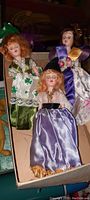 Three old weighted dolls with original colorful clothing, posed seated in a box.