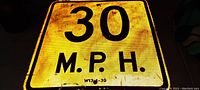 Photo showing front reflective surface of vintage 30 MPH metal street sign with visible dirt and wear on yellow background and black text.