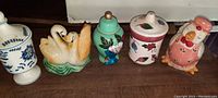 Blue and white floral decorated vessel, swan figures, green urn, pink floral lidded container, pink chicken figurine all displayed together