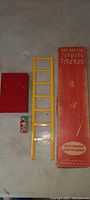 Photo of yellow metal ladder, red metal base, and tin fireman figure next to original red box