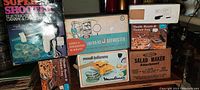 Several vintage kitchen appliance boxes arranged showing brand names and product details including an electric canapé shooter and infra-red defroster.