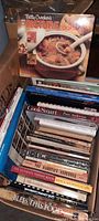 View of a plastic crate filled with various cooking and food related books showing titles like Betty Crocker's Picture Cookbook and The Ultimate Shrimp Book.