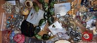 Overhead view showing green faceted bead necklace, silver-tone earrings, some rings, and mixed small jewelry pieces spread out.