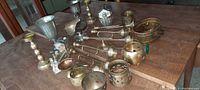 Wide view of vintage brass and metal items showing candle holders, small pots, and accessories arranged on a wooden table.