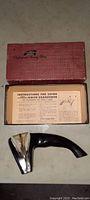 Vintage Cutco tool sharpener and original box with instruction sheet inside, placed on floor.