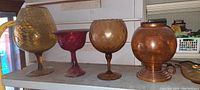 Four large goblet-style glassware items on shelf, showing colors and texture details including hammered and smooth finishes