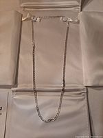 Sterling silver chain necklace laid flat on a white satin-like display surface, showing length and overall design.