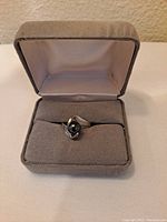 Ring displayed in a gray velvet jewelry box on a light fabric surface, showing the front angled view of the black sphere centered on the band.