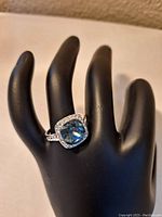Ring displayed on a black hand mannequin showcasing the blue crystal and clear crystal halo.