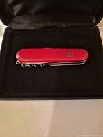 Front side of closed red Victorinox Swiss Army multi-tool showing emblem on handle, resting on black velvet.