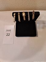 Front view of 5 vintage silver and gold tone tie clips displayed on black stand showing different decorative designs and varying lengths from 1 1/2 to 2 inches.