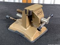 Side view of the gold-colored tabletop vice showing Chevrolet decal, adjustment screws, and rubber suction mount base.