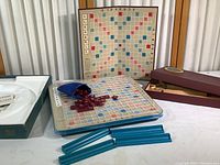 View showing both the vintage wooden Scrabble game box and game board standing vertically and the deluxe edition game board with letter tiles and racks.