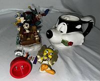 Photo showing Disney Christmas ornament with Mickey, Goofy, Pluto, and Donald, Tweety Bird ornament, and Pepe Le Pew mug in white and black ceramic with rose.