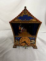 Full front view of the Disney Pinocchio musical wall clock shaped like a stage theater, showing Pinocchio and Jiminy Cricket with a wooden village backdrop and intricate details.