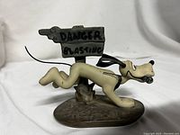 Side view showing Pluto running past the wooden sign with 'Danger Blasting' text and holding dynamite stick in mouth.