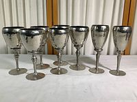 All eight hammered pewter goblets arranged in a single row on white surface