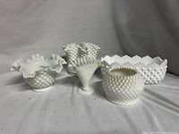 Five white milk glass collectible items including hobnail and ruffled edge pieces arranged on a white surface, showing distinctive hobnail and ruffled rim textures.