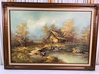 Front view of the large original painting showcasing a rustic barn and stream in a wooded landscape with autumn trees, all framed ornately in gold-bronze wood.