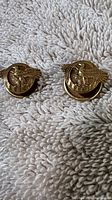 Pair of WWII Ruptured Duck Honorable Discharge lapel cufflinks on textured light-colored fabric showing the gold-tone eagle and wreath design.