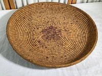 Top-down view of large handmade woven basket woven with fine fibers showing concentric spiral pattern with some purple accents.