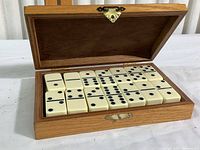 Open wooden box showing 28 ivory domino tiles neatly arranged in fabric lined compartment.