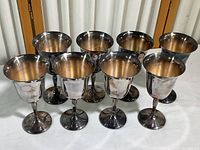 Front angled view of the eight silver goblets showing size, shape and tarnish on the surfaces indicating need for polishing.