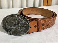 Tooled brown leather belt rolled with the oval cast metal buckle showing a raised fish design.