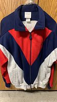 Front view of vintage Adidas track jacket showing color blocking in navy blue, red, and light gray.