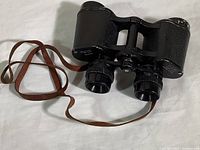 Full view of the binoculars alongside the attached brown leather strap.