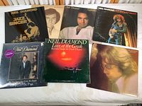 Top view of seven Neil Diamond vinyl LP albums arranged side by side and overlapping, showcasing album artwork featuring portraits and live photo imagery.